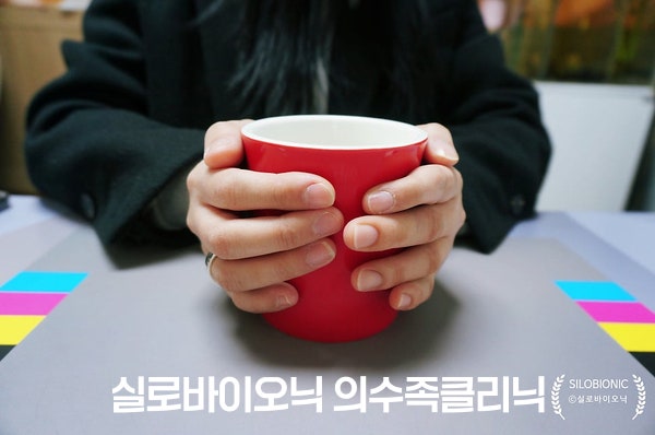 실리콘 손가락 의수를 낀 손으로 빨간 컵을 감싸 쥔 모습