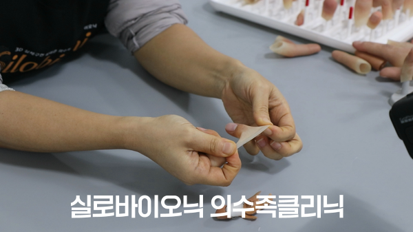 직원이 얇은 실리콘 의수 가장자리를 손으로 늘려 보이는 모습